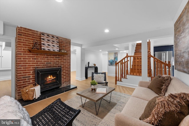 living area featuring baseboards, stairway, wood finished floors, a brick fireplace, and recessed lighting