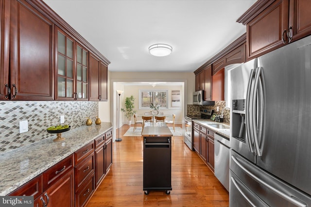 kitchen with light stone counters, hardwood / wood-style flooring, a sink, appliances with stainless steel finishes, and glass insert cabinets