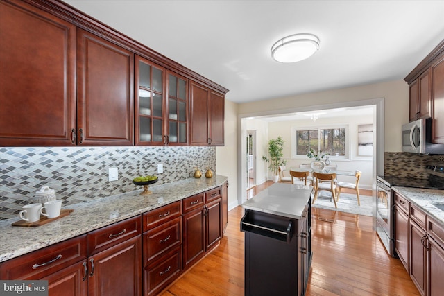 kitchen featuring glass insert cabinets, light wood-style flooring, appliances with stainless steel finishes, and decorative backsplash