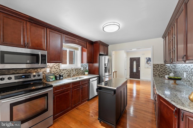 kitchen featuring decorative backsplash, a center island, stainless steel appliances, light wood-style floors, and a sink