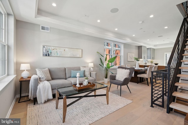 living area featuring light wood-type flooring, a tray ceiling, visible vents, and stairway