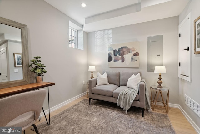 sitting room with electric panel, visible vents, baseboards, and wood finished floors