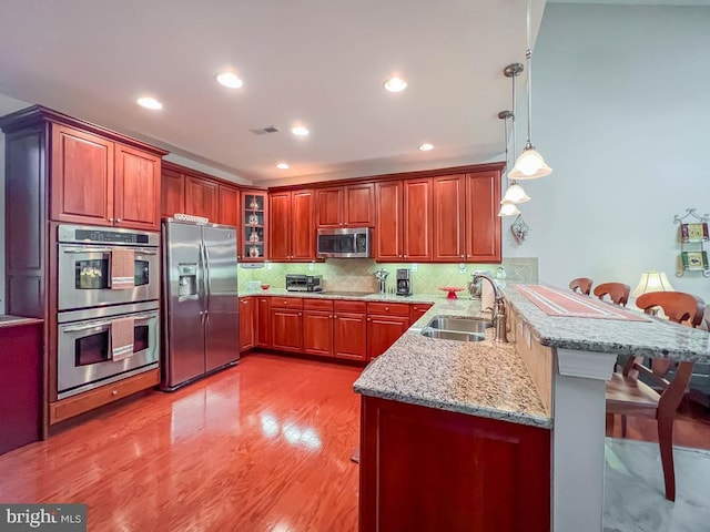 kitchen featuring glass insert cabinets, appliances with stainless steel finishes, a breakfast bar, a peninsula, and a sink