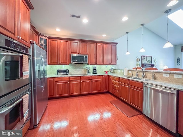 kitchen with a sink, visible vents, hanging light fixtures, appliances with stainless steel finishes, and light stone countertops