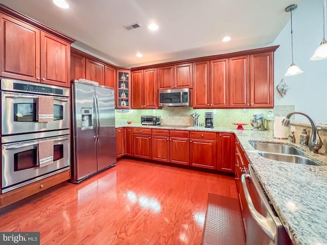 kitchen featuring decorative light fixtures, visible vents, appliances with stainless steel finishes, a sink, and light stone countertops