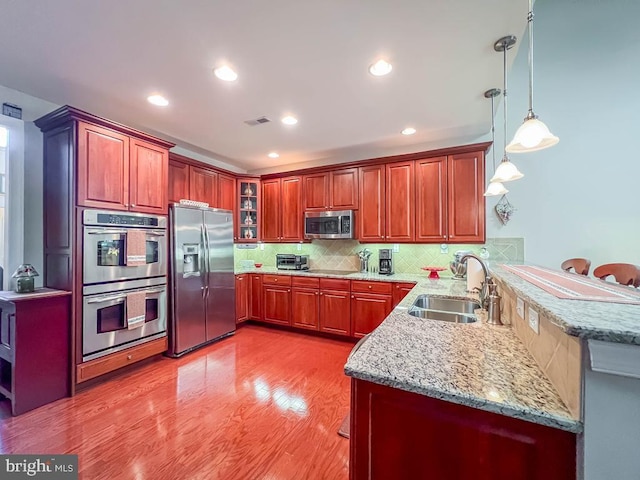 kitchen with hanging light fixtures, appliances with stainless steel finishes, glass insert cabinets, a sink, and a peninsula