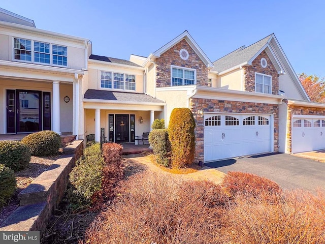 view of front facade featuring driveway, covered porch, an attached garage, and stone siding