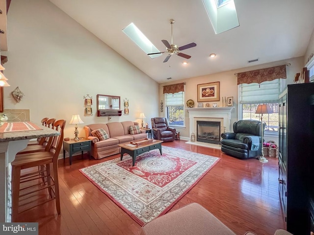 living room with a skylight, visible vents, a glass covered fireplace, high vaulted ceiling, and hardwood / wood-style flooring