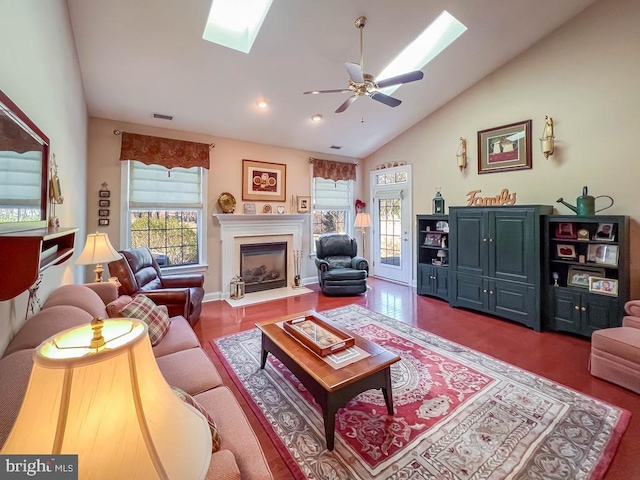 living room with a skylight, visible vents, a ceiling fan, a glass covered fireplace, and high vaulted ceiling