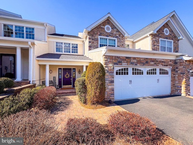 view of front of house featuring an attached garage, covered porch, driveway, stone siding, and stucco siding