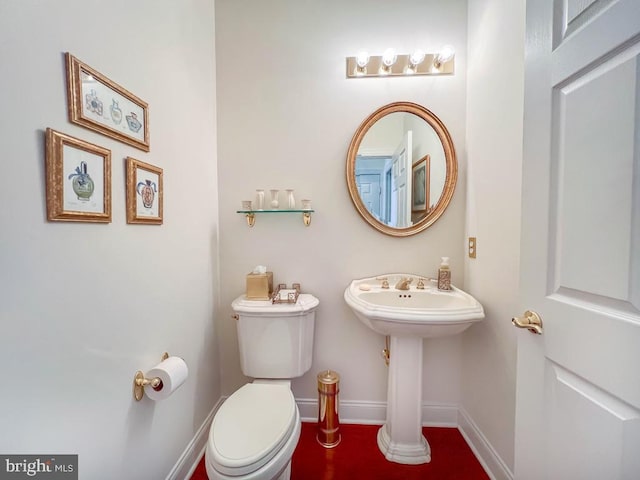 half bath with toilet, baseboards, and a sink