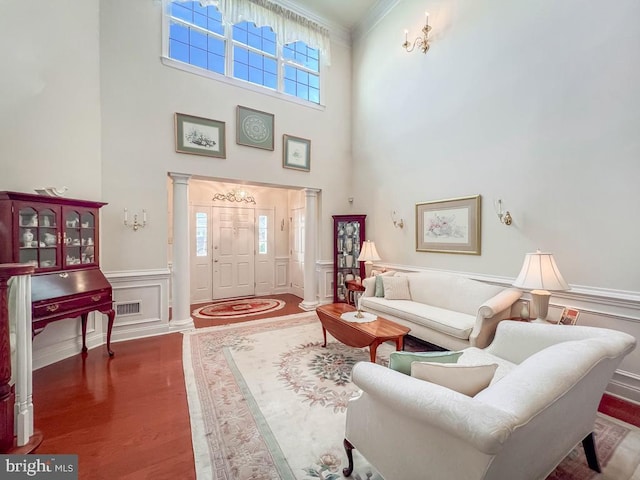 living room with a decorative wall, visible vents, ornamental molding, wainscoting, and ornate columns