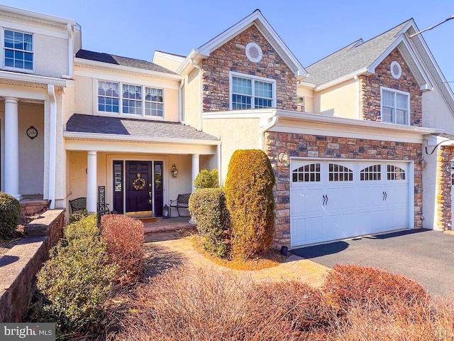 view of front of home with driveway, a garage, stone siding, covered porch, and stucco siding