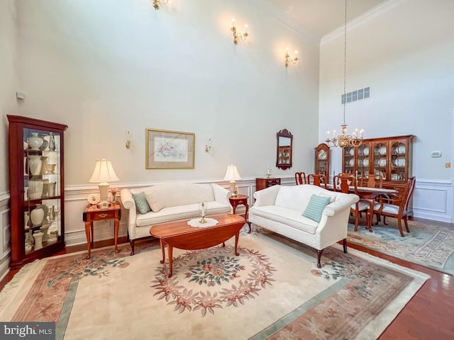 living room with a notable chandelier, a decorative wall, wood finished floors, visible vents, and crown molding