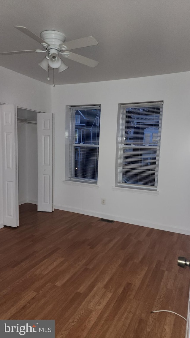 unfurnished bedroom with dark wood-type flooring, a closet, a ceiling fan, and baseboards