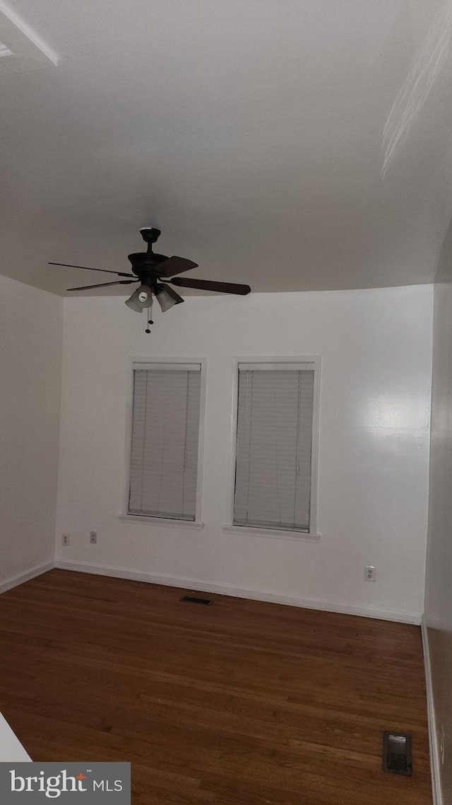 unfurnished room with dark wood-style flooring, visible vents, ceiling fan, and baseboards