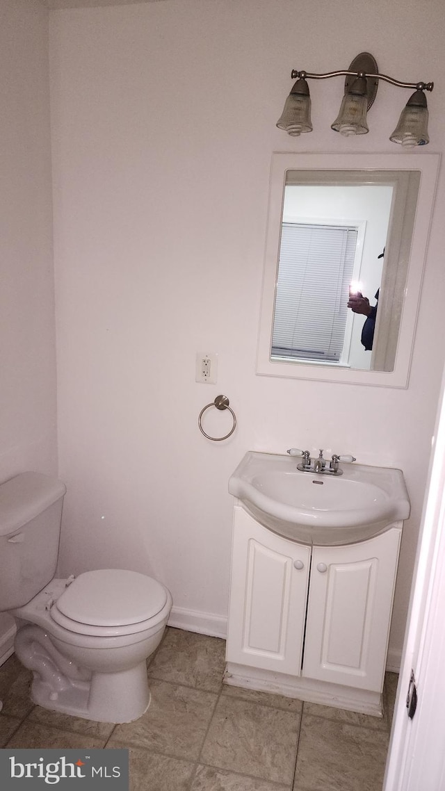 half bathroom featuring toilet, baseboards, and vanity