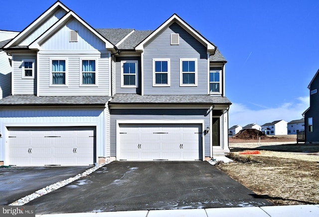 multi unit property with a garage, driveway, and roof with shingles