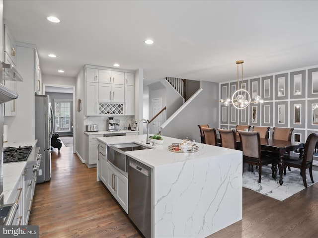 kitchen with light stone counters, a kitchen island with sink, stainless steel appliances, a sink, and hanging light fixtures