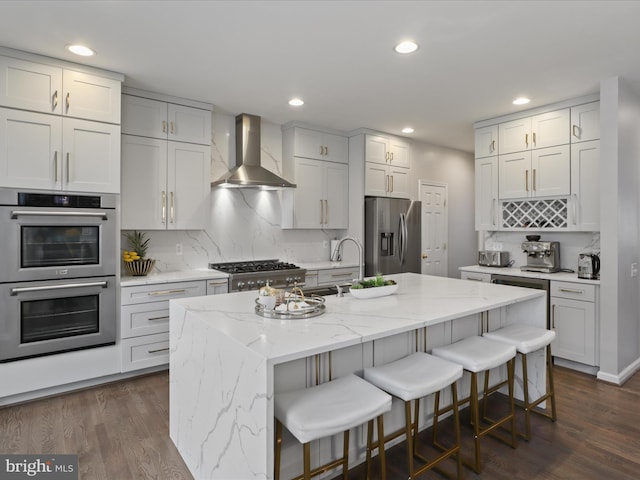 kitchen featuring appliances with stainless steel finishes, white cabinets, an island with sink, and wall chimney exhaust hood