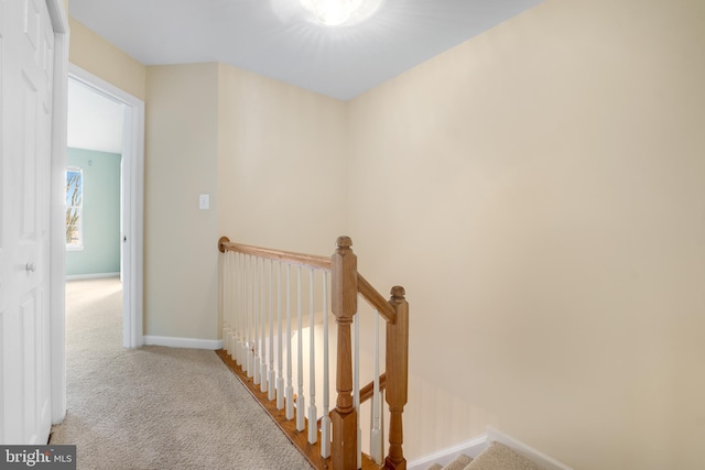 corridor featuring carpet floors, baseboards, and an upstairs landing