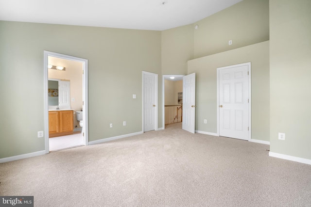 unfurnished bedroom featuring high vaulted ceiling, light carpet, connected bathroom, and baseboards