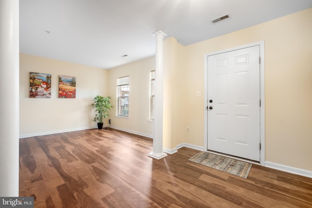 foyer entrance featuring visible vents, decorative columns, baseboards, and wood finished floors