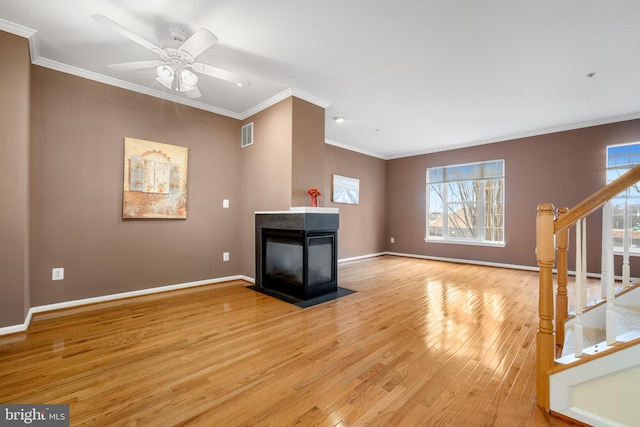 unfurnished living room with light wood-style flooring, a multi sided fireplace, visible vents, ornamental molding, and stairway