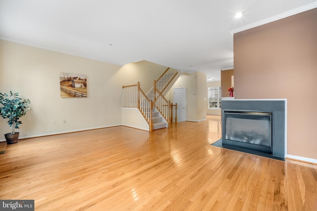 unfurnished living room with wood finished floors, a multi sided fireplace, baseboards, stairway, and crown molding