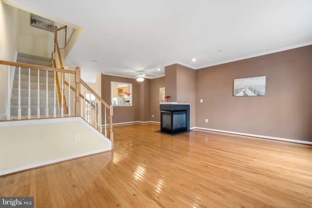 unfurnished living room featuring hardwood / wood-style flooring, stairs, crown molding, and a multi sided fireplace