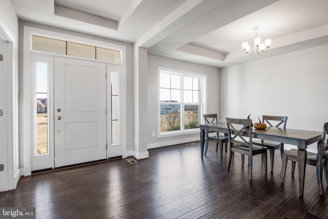 foyer with dark wood-style floors, a notable chandelier, a raised ceiling, and baseboards