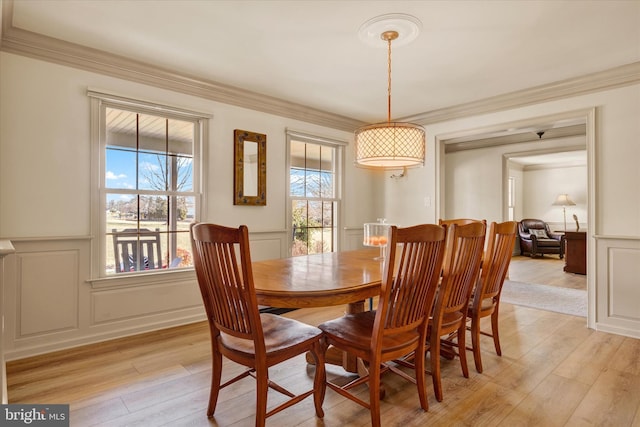 dining space featuring ornamental molding, a wealth of natural light, a decorative wall, and light wood-style flooring