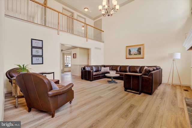 living area featuring a chandelier, light wood-type flooring, visible vents, and a towering ceiling