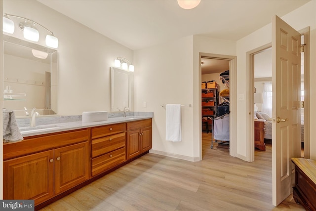 ensuite bathroom featuring double vanity, a walk in closet, a sink, and wood finished floors