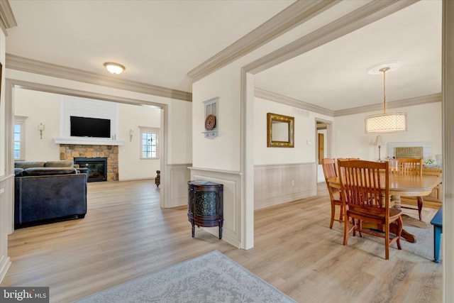 dining space with light wood finished floors, crown molding, a stone fireplace, and wainscoting