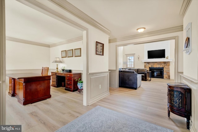 interior space featuring a wainscoted wall, a stone fireplace, ornamental molding, and light wood-style flooring