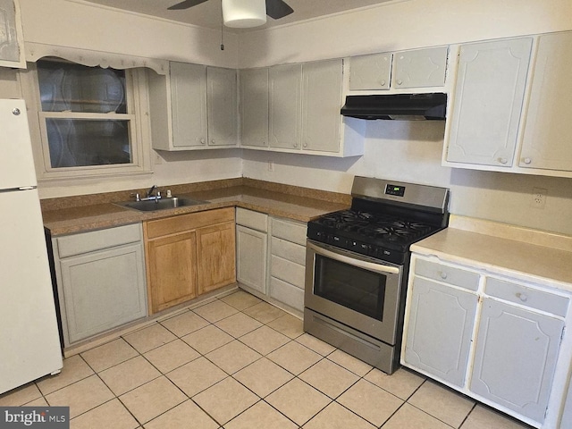 kitchen featuring light tile patterned floors, under cabinet range hood, a sink, freestanding refrigerator, and gas range