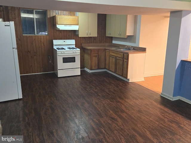 kitchen featuring white appliances, under cabinet range hood, dark wood-style floors, and a sink