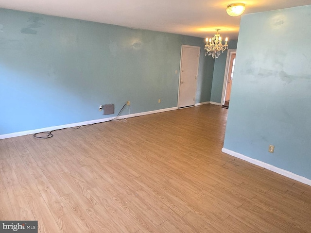 empty room featuring baseboards, a chandelier, and wood finished floors