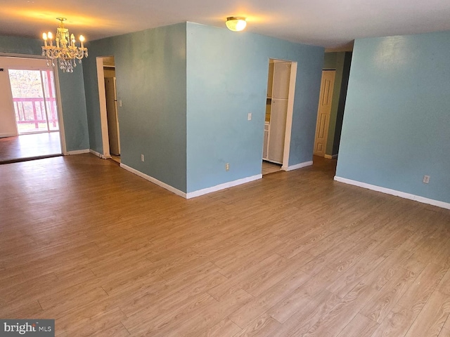 spare room with a notable chandelier, baseboards, and wood finished floors