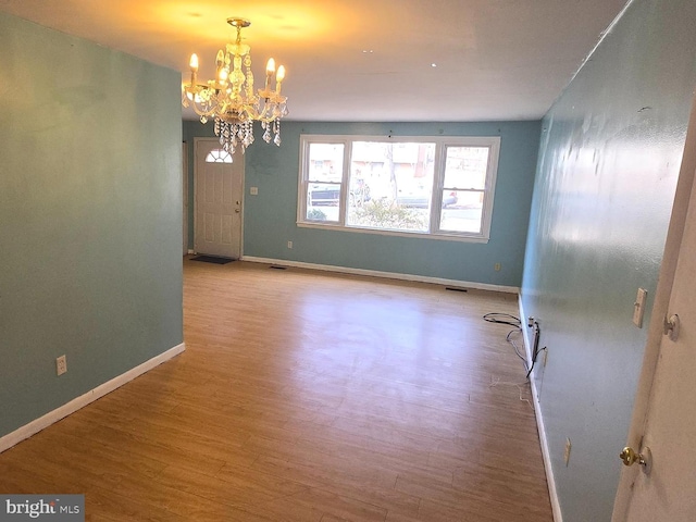 empty room with an inviting chandelier, wood finished floors, visible vents, and baseboards