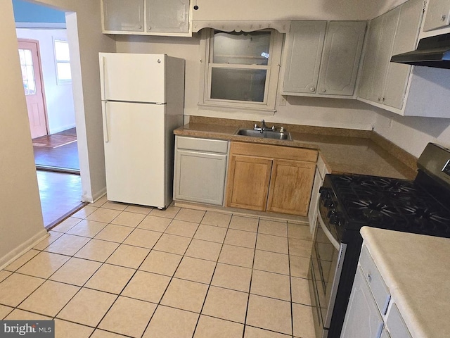 kitchen featuring gas stove, freestanding refrigerator, light tile patterned flooring, a sink, and under cabinet range hood