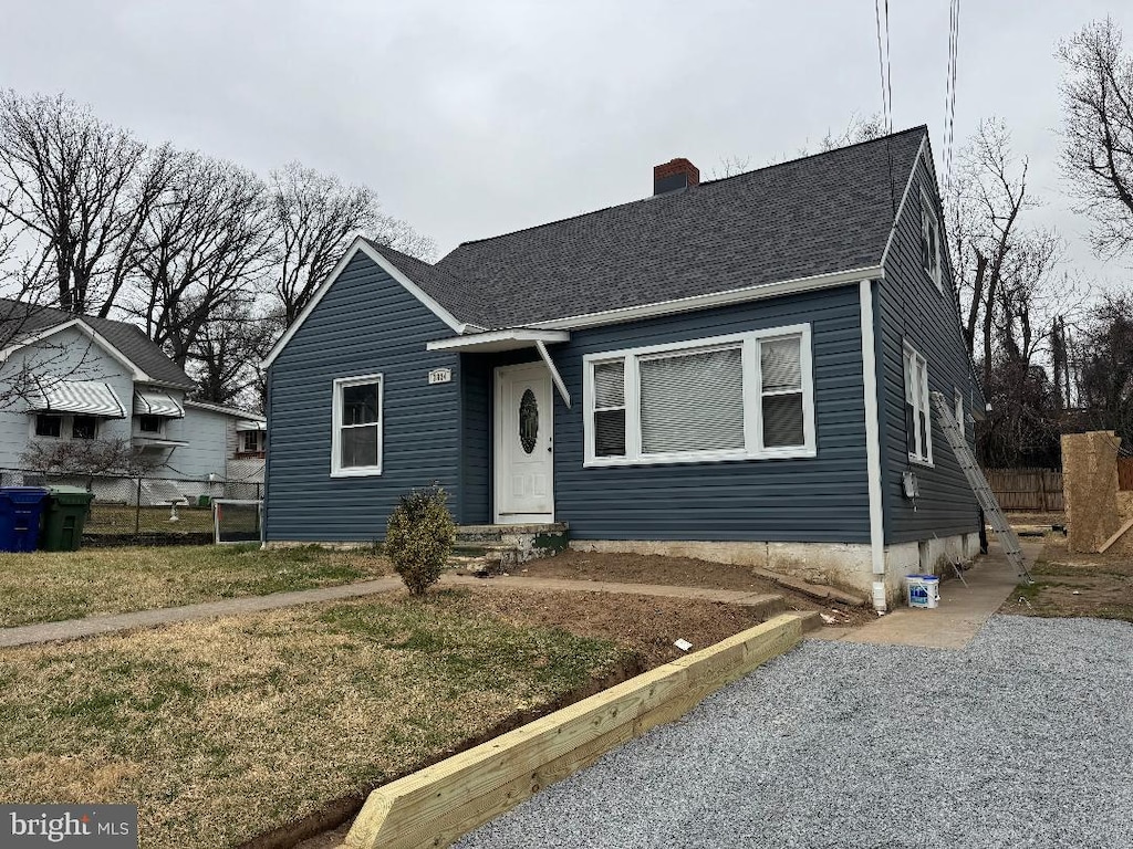 view of front facade with a shingled roof, a chimney, and fence