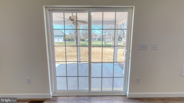 doorway to outside featuring a ceiling fan, visible vents, baseboards, and wood finished floors