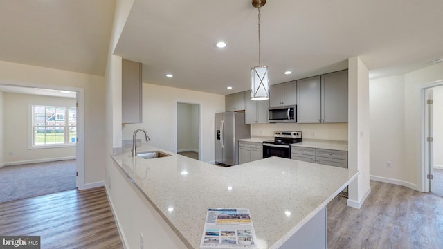 kitchen featuring light stone counters, stainless steel appliances, hanging light fixtures, a sink, and a peninsula