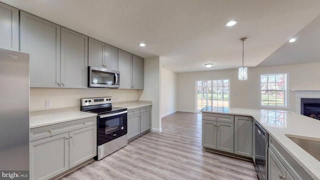 kitchen featuring appliances with stainless steel finishes, gray cabinets, hanging light fixtures, and open floor plan