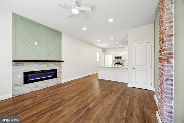 unfurnished living room featuring dark wood-type flooring, a high end fireplace, baseboards, and recessed lighting