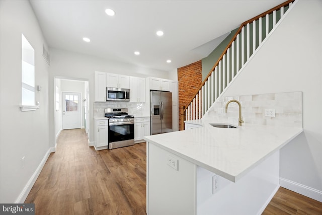 kitchen with stainless steel appliances, light countertops, white cabinets, a sink, and a peninsula