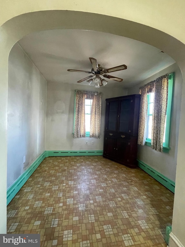 unfurnished bedroom with multiple windows, a baseboard heating unit, and arched walkways