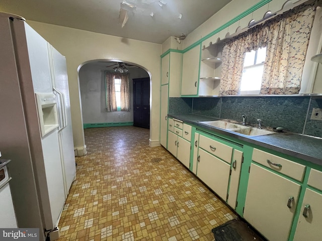 kitchen with arched walkways, white fridge with ice dispenser, dark countertops, and open shelves